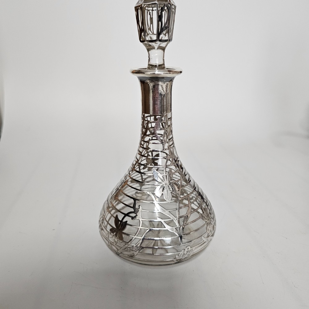 An early 20th-century glass decanter featuring an intricate sterling silver floral overlay and matching stopper.