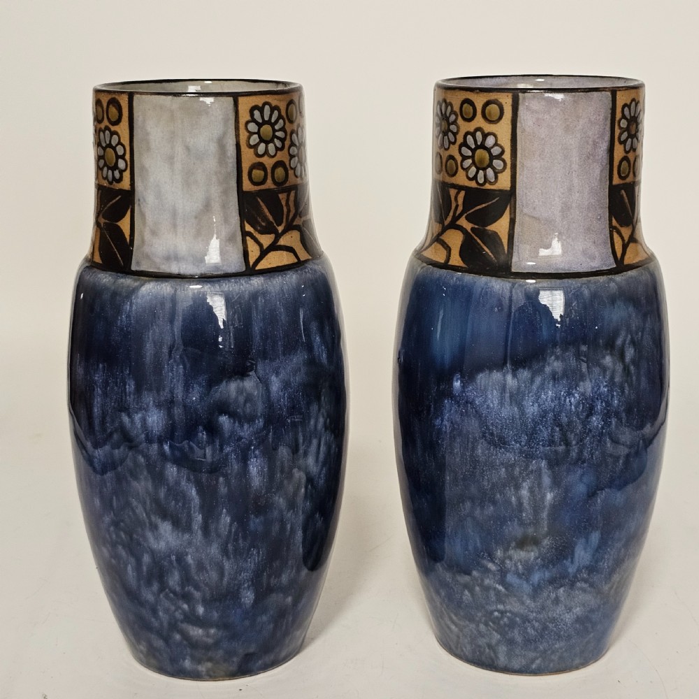 A pair of Royal Doulton stoneware vases featuring mottled blue glaze bodies and upper decorative bands with hand-painted floral motifs.