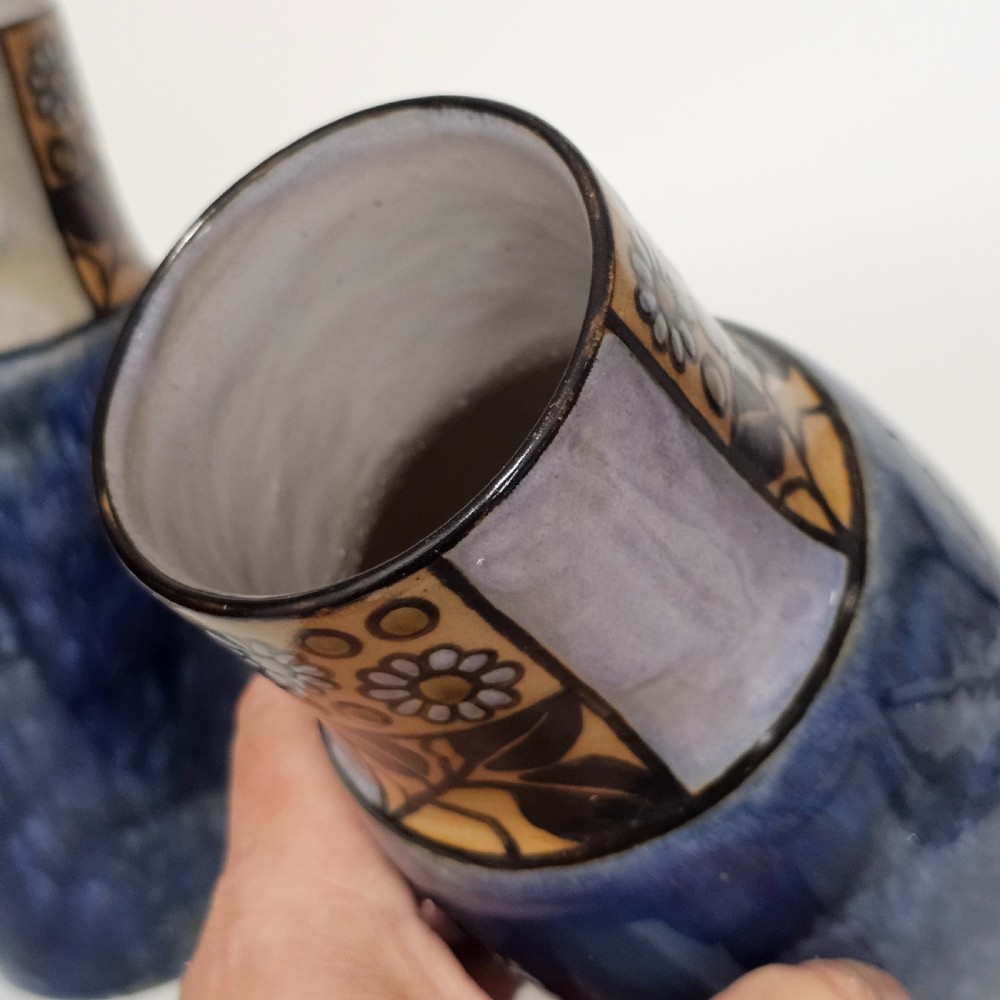 A pair of Royal Doulton stoneware vases featuring mottled blue glaze bodies and upper decorative bands with hand-painted floral motifs. View X