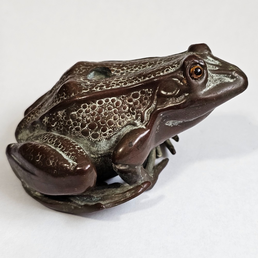 An antique cast bronze frog pen holder featuring textured skin details and inset glass eyes.