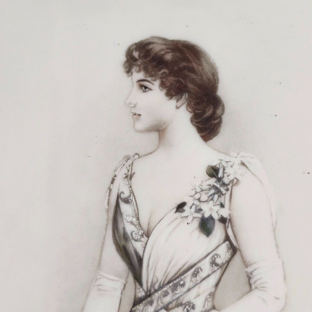 A rectangular framed porcelain plaque featuring a monochrome depiction of an Edwardian lady holding a fan within an ornate gilt frame. View II