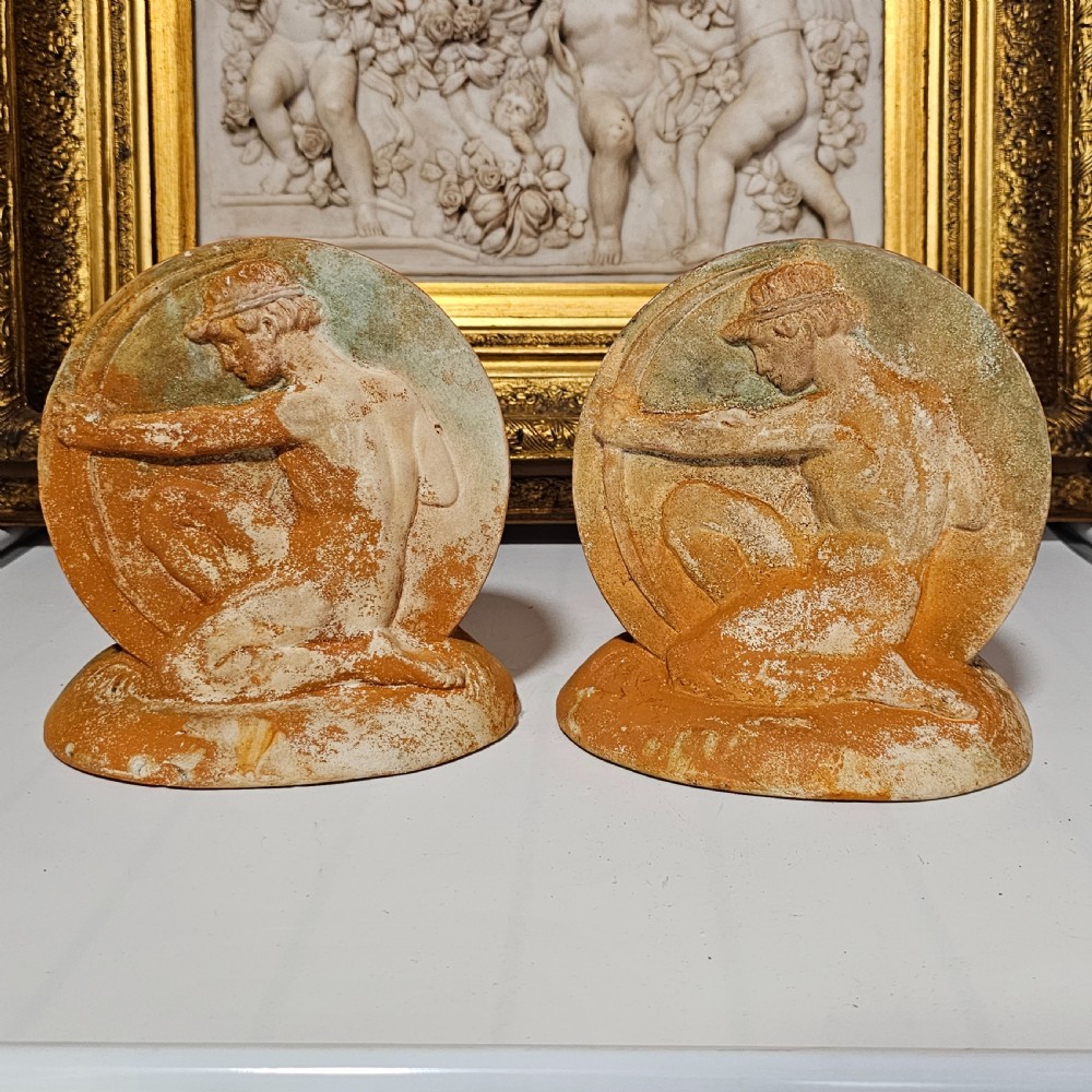 A pair of circular terracotta bookends depicting a kneeling archer with a drawn bow in relief sculpture with a distressed white wash finish.