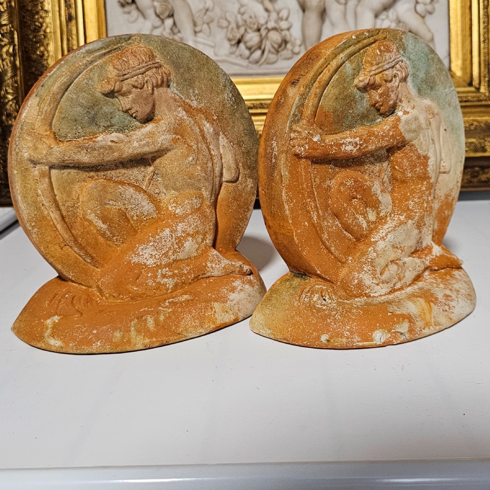 A pair of circular terracotta bookends depicting a kneeling archer with a drawn bow in relief sculpture with a distressed white wash finish. View II