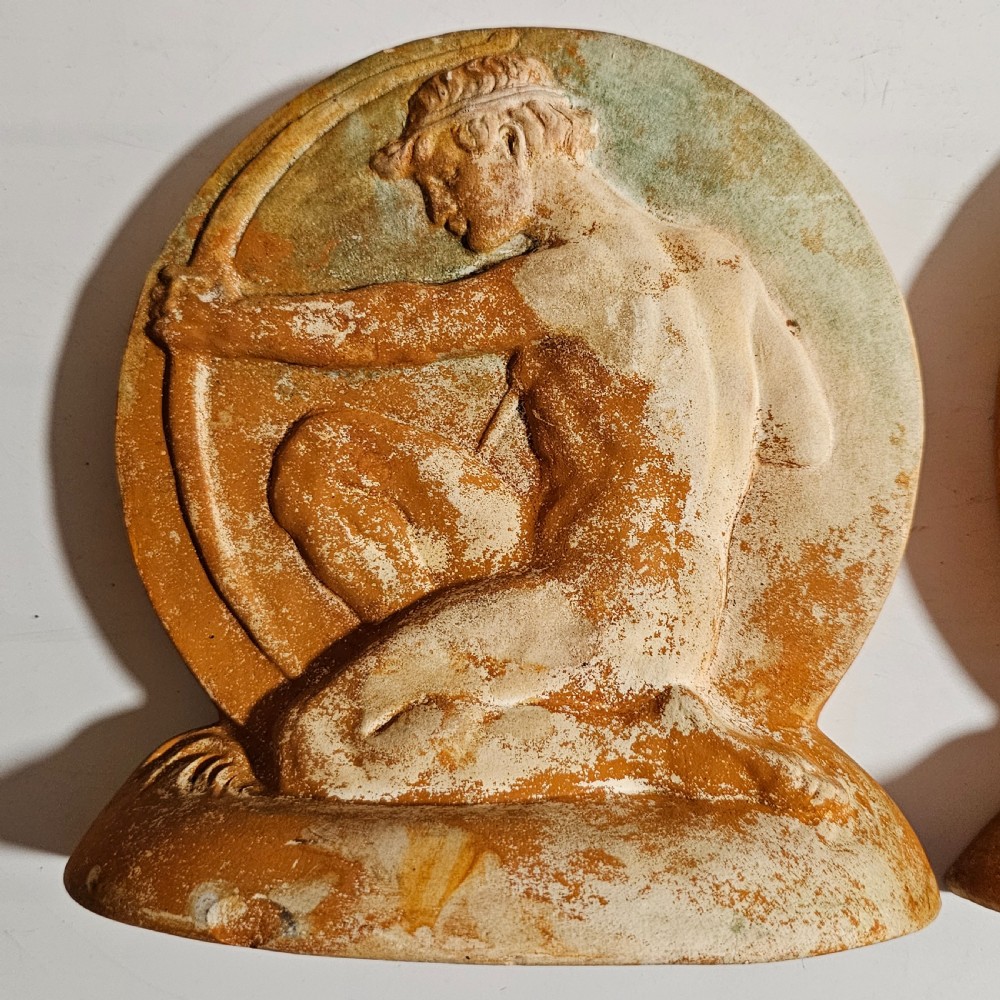 A pair of circular terracotta bookends depicting a kneeling archer with a drawn bow in relief sculpture with a distressed white wash finish. View III