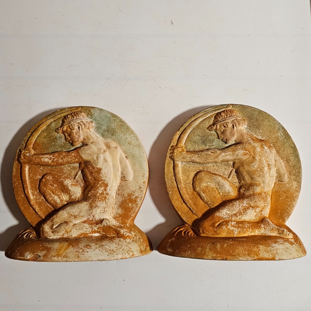 A pair of circular terracotta bookends depicting a kneeling archer with a drawn bow in relief sculpture with a distressed white wash finish. View VII