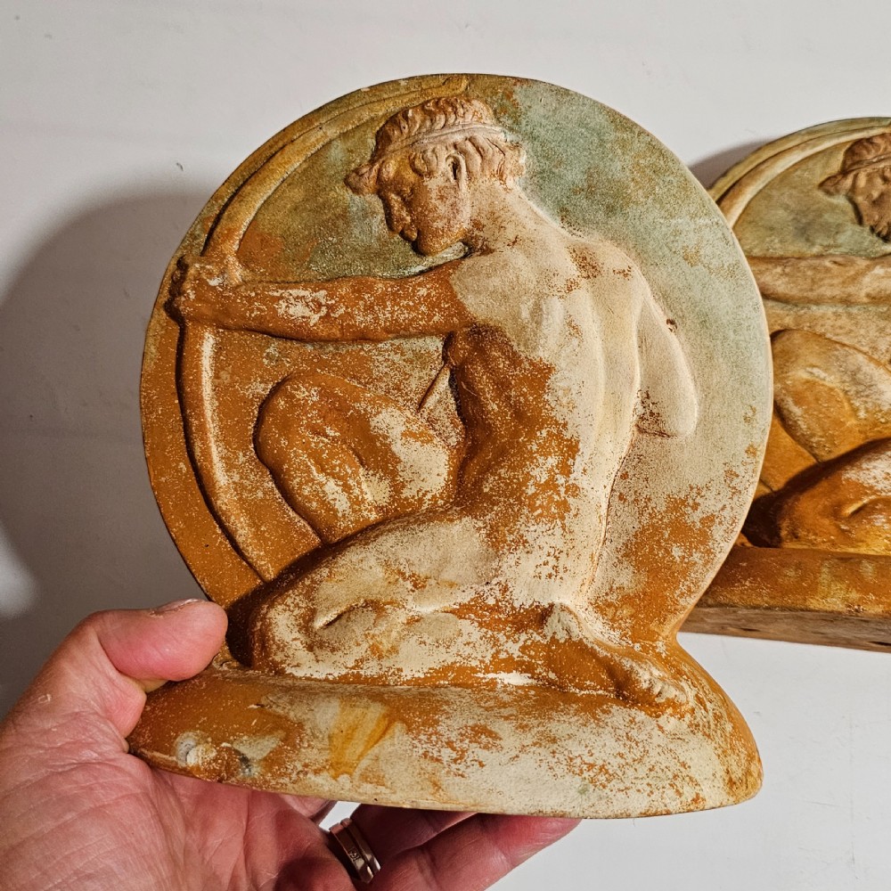 A pair of circular terracotta bookends depicting a kneeling archer with a drawn bow in relief sculpture with a distressed white wash finish. View VIII