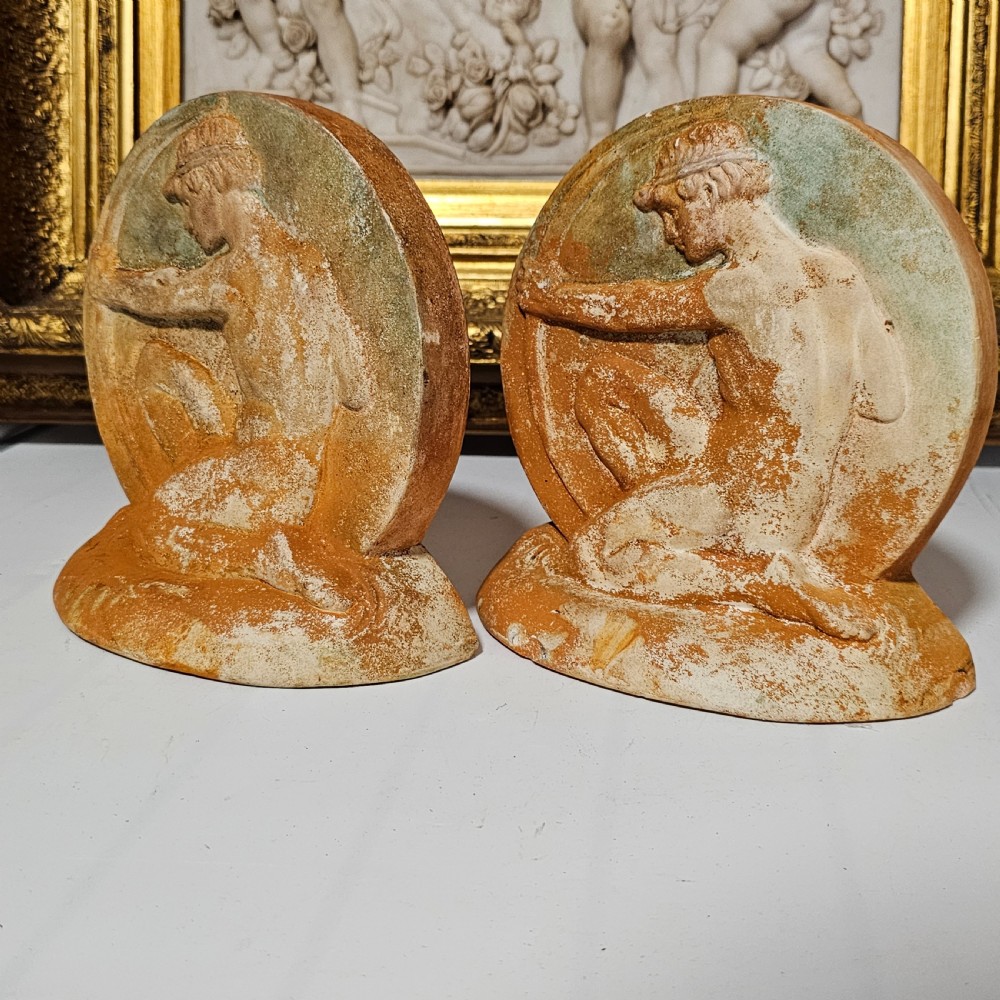 A pair of circular terracotta bookends depicting a kneeling archer with a drawn bow in relief sculpture with a distressed white wash finish. View XI