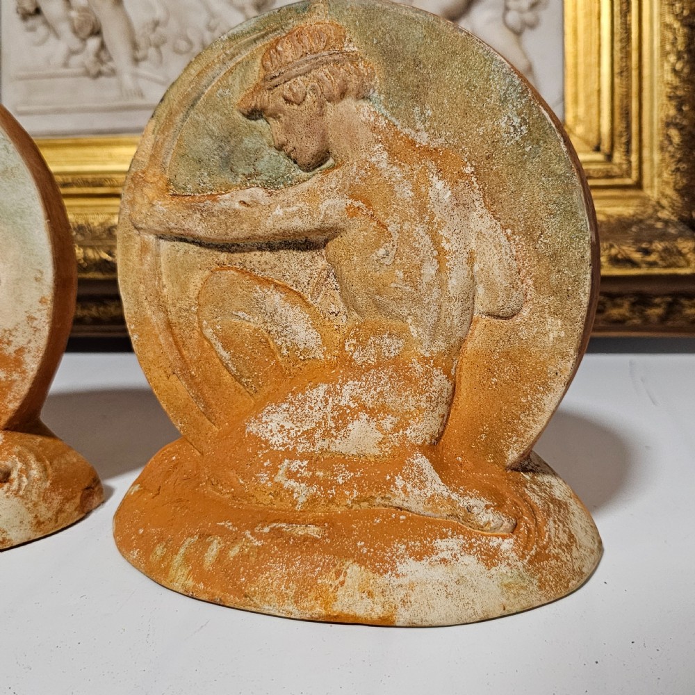 A pair of circular terracotta bookends depicting a kneeling archer with a drawn bow in relief sculpture with a distressed white wash finish. View XII