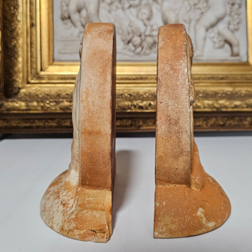 A pair of circular terracotta bookends depicting a kneeling archer with a drawn bow in relief sculpture with a distressed white wash finish. View XIII