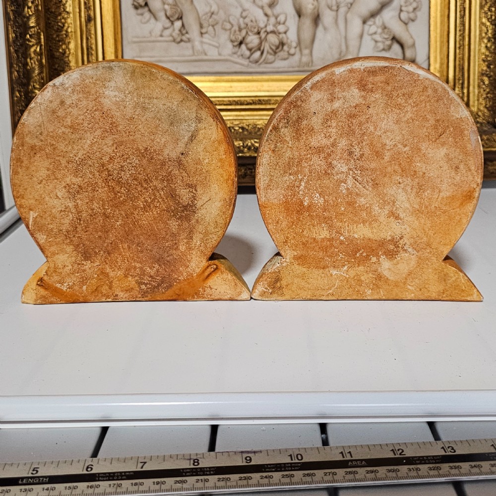 A pair of circular terracotta bookends depicting a kneeling archer with a drawn bow in relief sculpture with a distressed white wash finish. View XIV