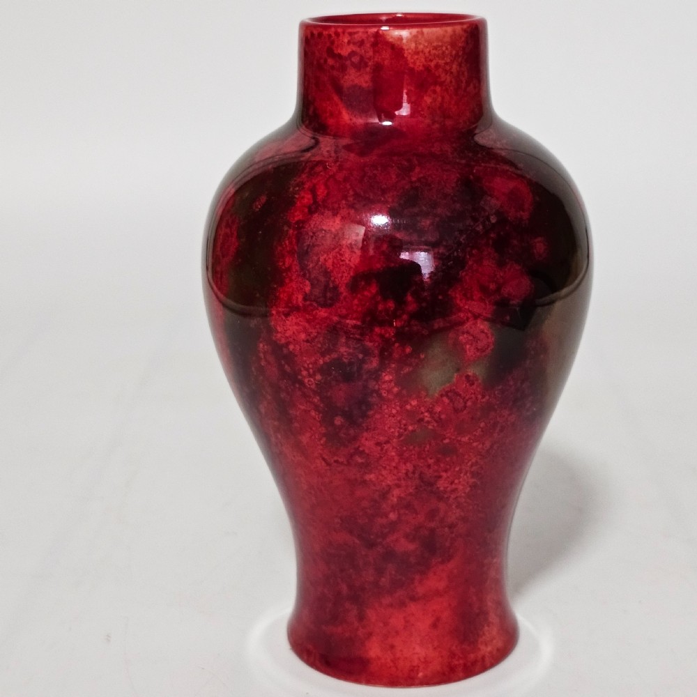 A glossy ceramic vase featuring a mottled flambe glaze transitioning from deep crimson red to dark tones at the neck. View VI