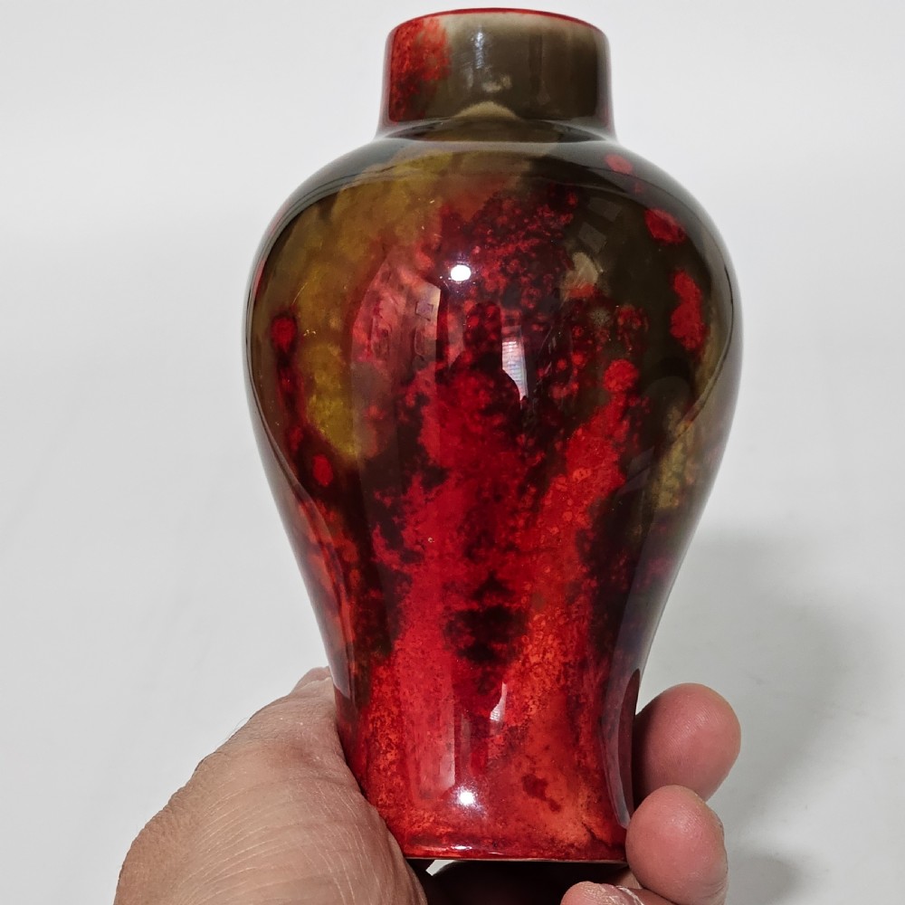 A glossy ceramic vase featuring a mottled flambe glaze transitioning from deep crimson red to dark tones at the neck. View X
