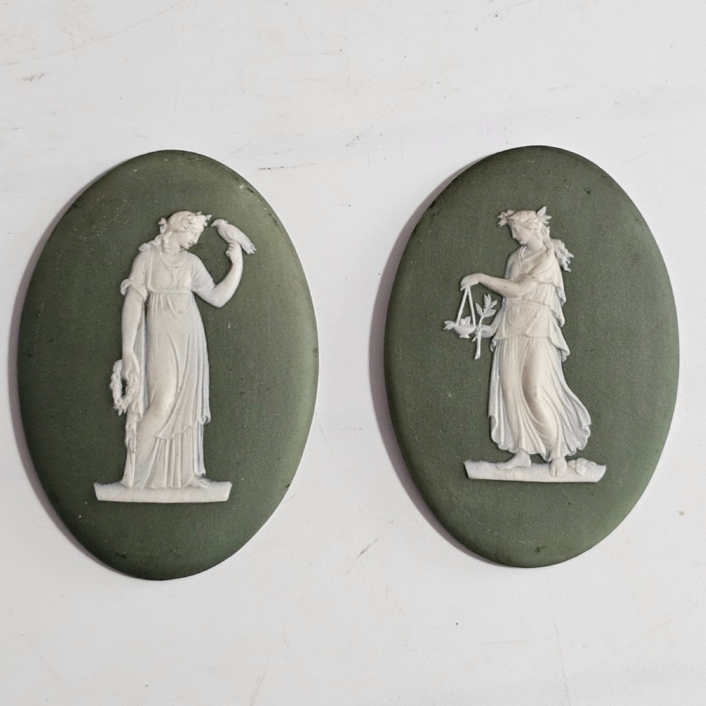 A pair of oval sage green stoneware plaques decorated with raised white relief figures in classical drapery.