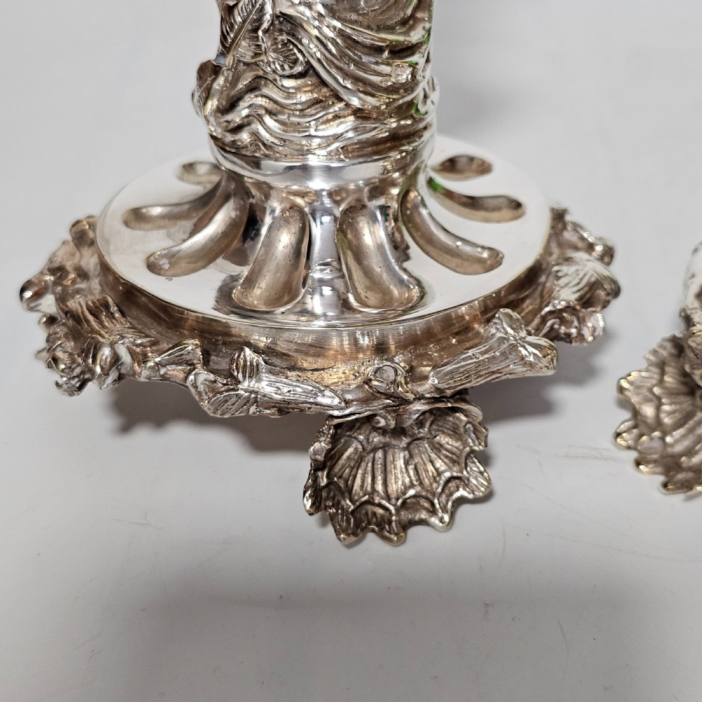A pair of antique silver-plated candlesticks featuring seated cherub figures supporting the candle nozzles above circular scrolled bases. View VIII