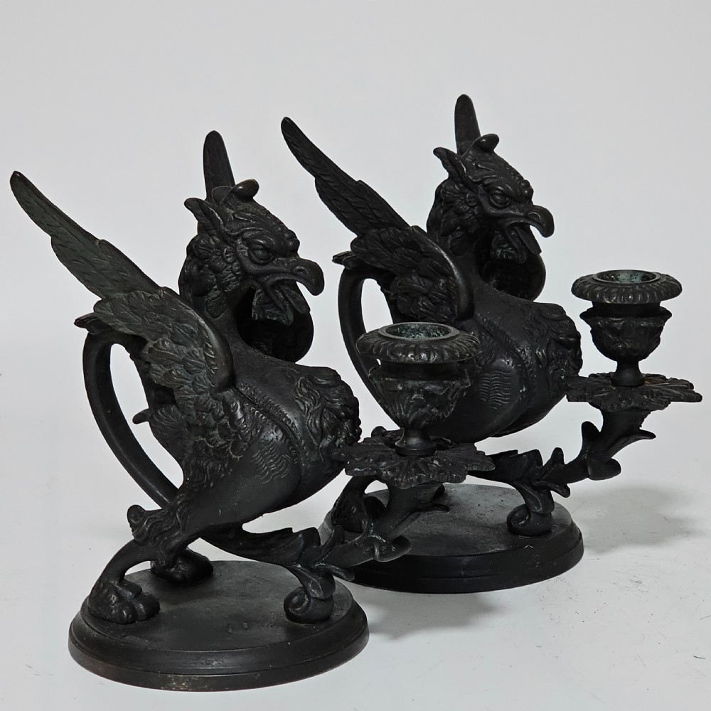 A pair of heavy dark bronze chambersticks featuring mythical griffin figures holding candle nozzles.