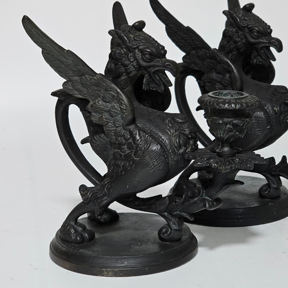 A pair of heavy dark bronze chambersticks featuring mythical griffin figures holding candle nozzles. View II