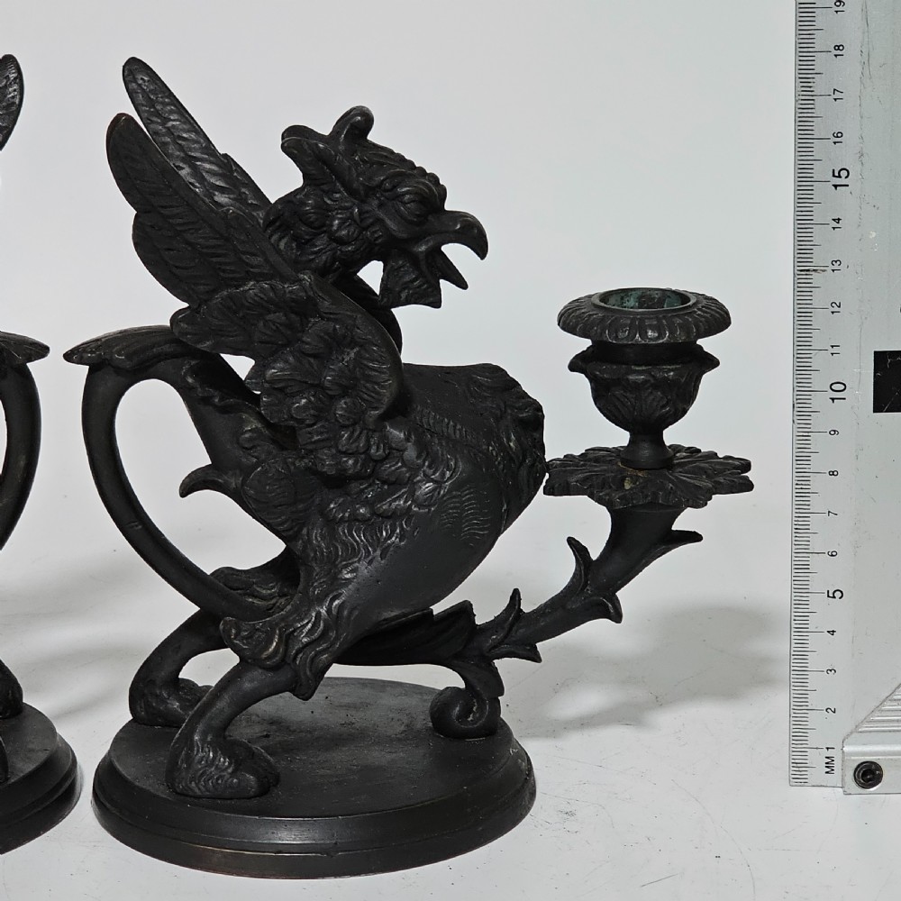 A pair of heavy dark bronze chambersticks featuring mythical griffin figures holding candle nozzles. View V