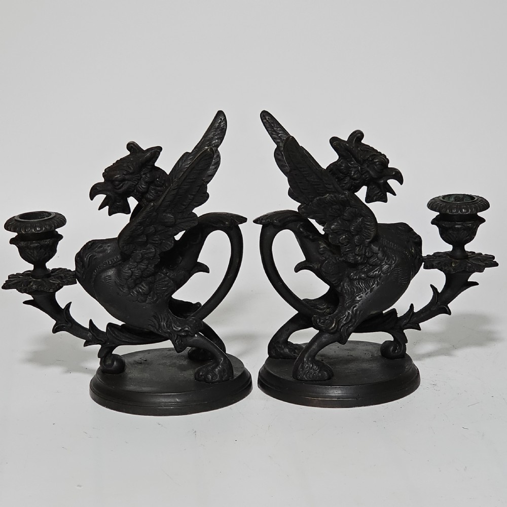 A pair of heavy dark bronze chambersticks featuring mythical griffin figures holding candle nozzles. View VI