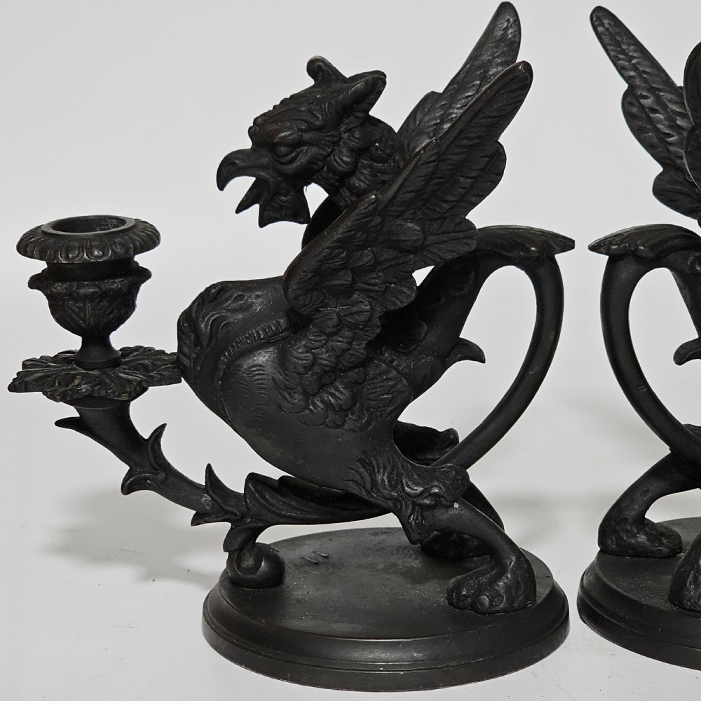 A pair of heavy dark bronze chambersticks featuring mythical griffin figures holding candle nozzles. View VII