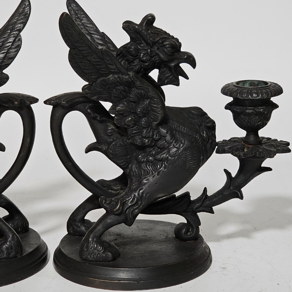 A pair of heavy dark bronze chambersticks featuring mythical griffin figures holding candle nozzles. View VIII