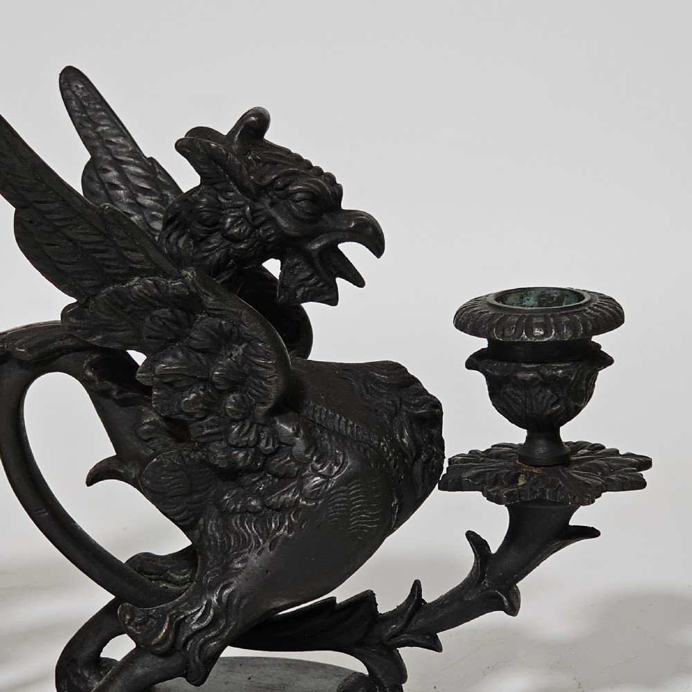 A pair of heavy dark bronze chambersticks featuring mythical griffin figures holding candle nozzles. View IX