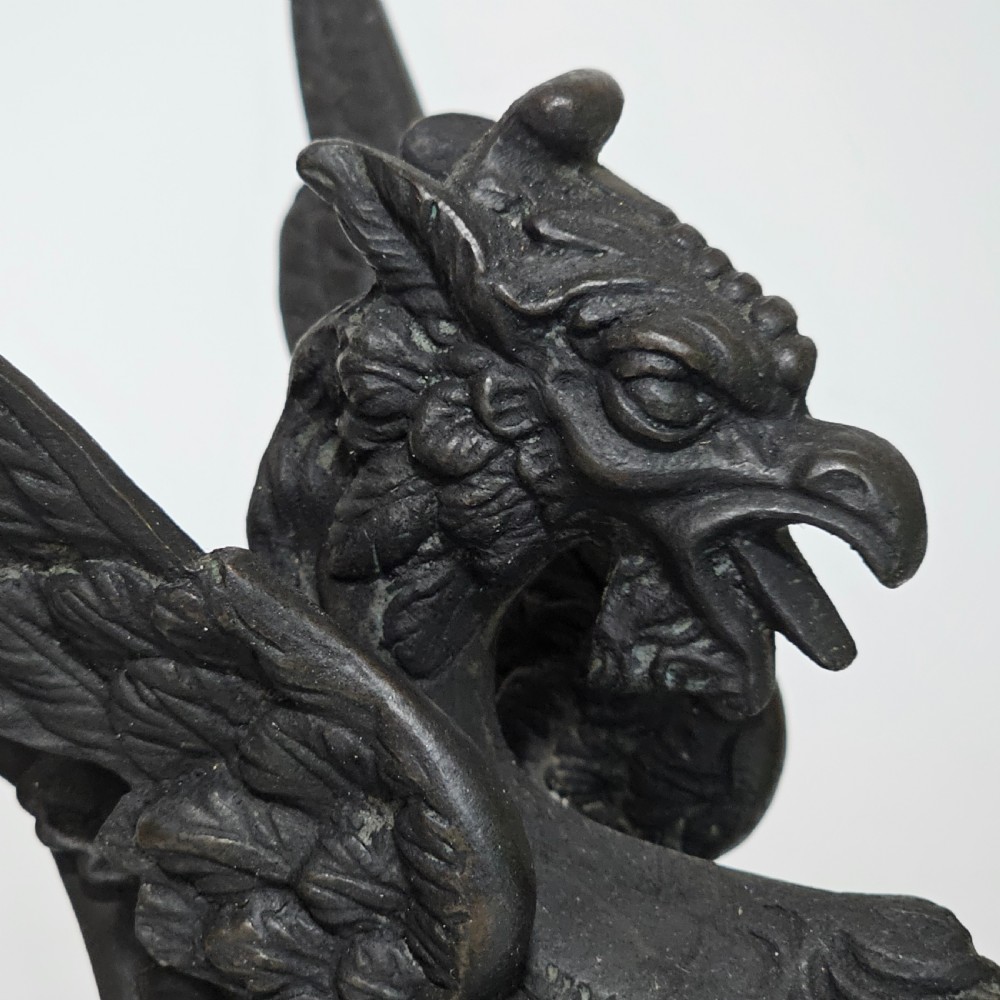 A pair of heavy dark bronze chambersticks featuring mythical griffin figures holding candle nozzles. View X