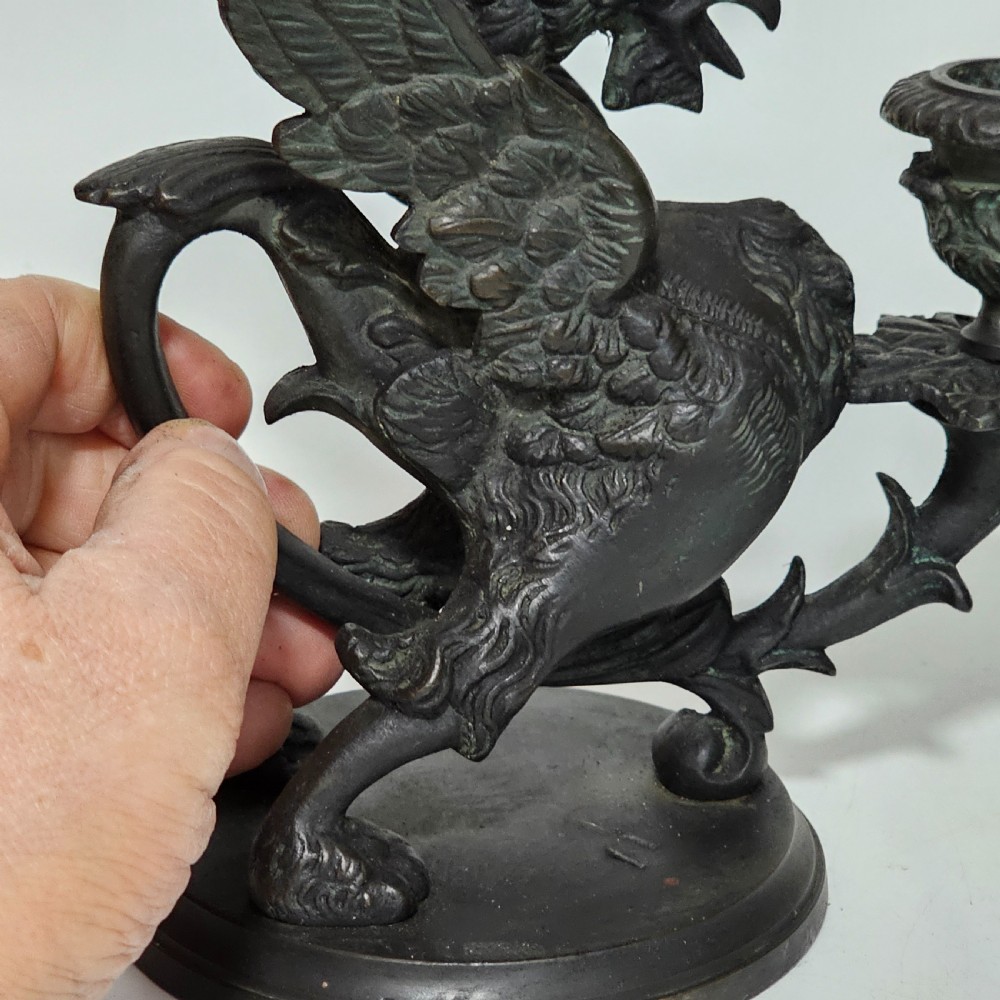 A pair of heavy dark bronze chambersticks featuring mythical griffin figures holding candle nozzles. View XII