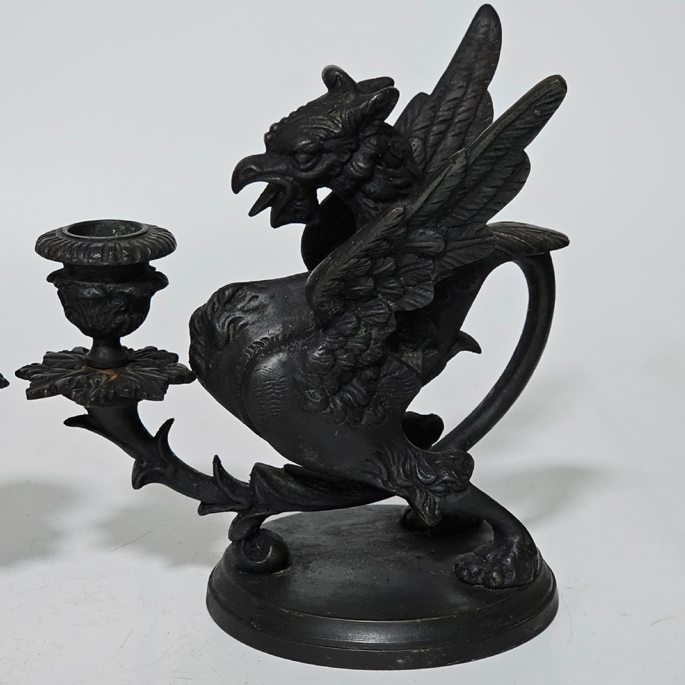 A pair of heavy dark bronze chambersticks featuring mythical griffin figures holding candle nozzles. View XIV