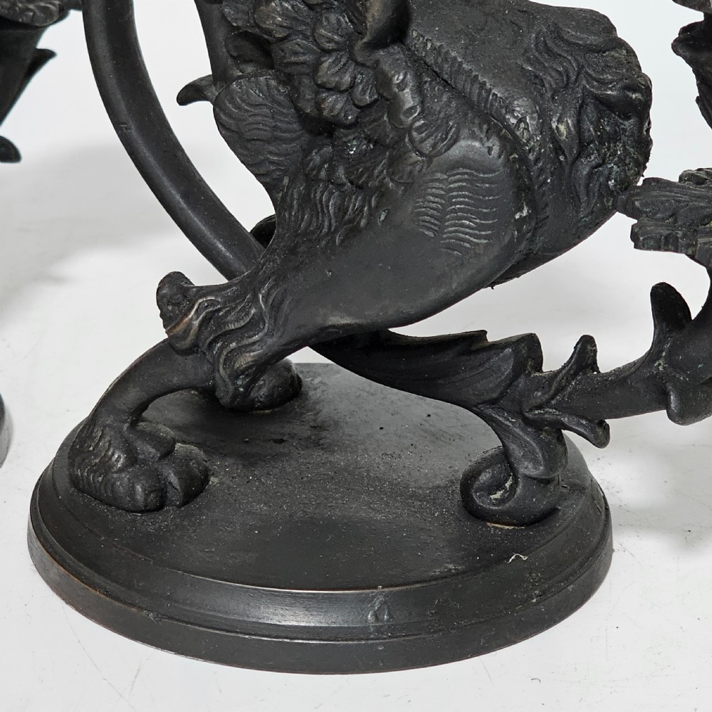 A pair of heavy dark bronze chambersticks featuring mythical griffin figures holding candle nozzles. View XVI