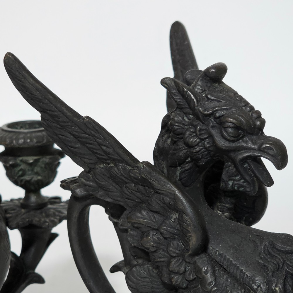 A pair of heavy dark bronze chambersticks featuring mythical griffin figures holding candle nozzles. View XVII