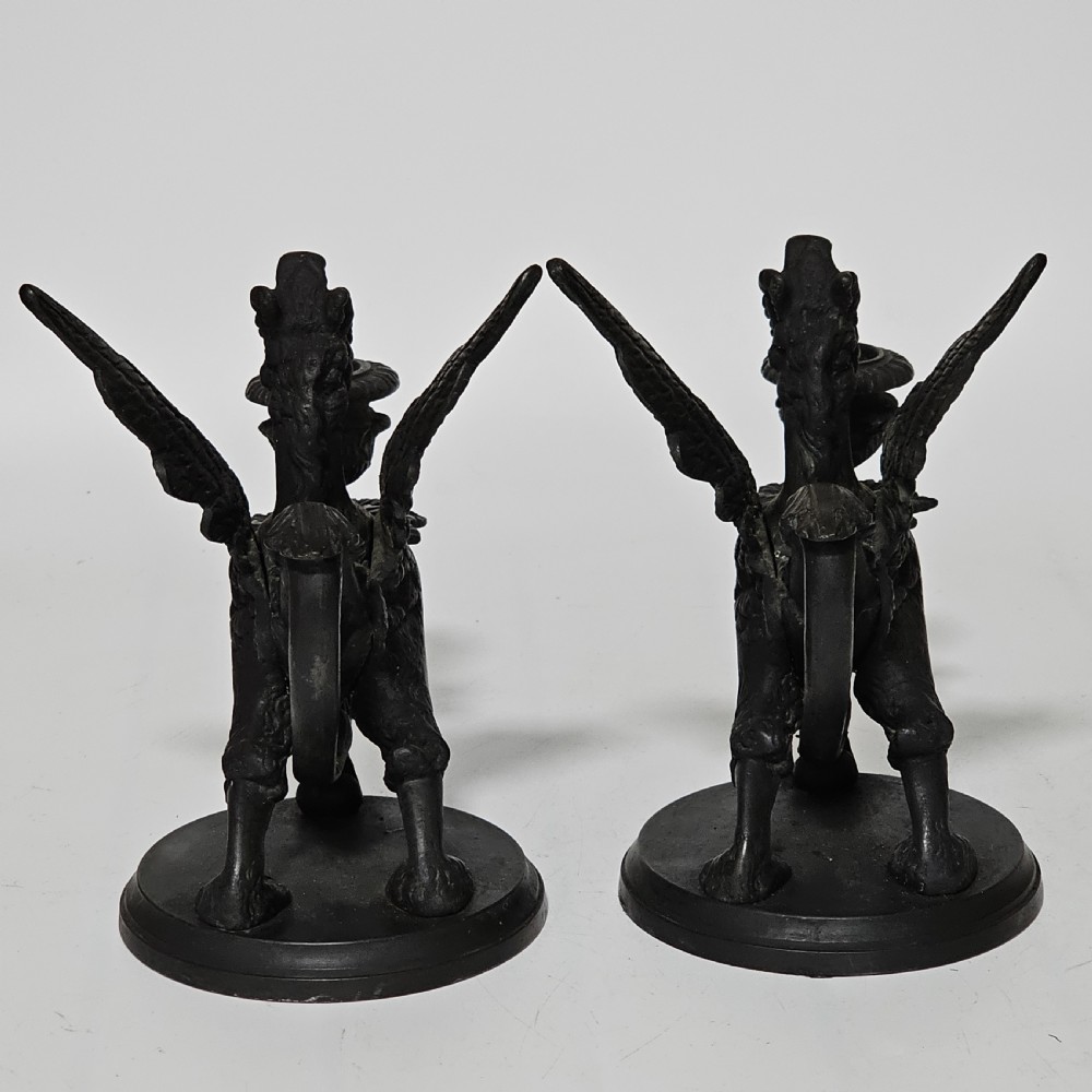 A pair of heavy dark bronze chambersticks featuring mythical griffin figures holding candle nozzles. View XIX