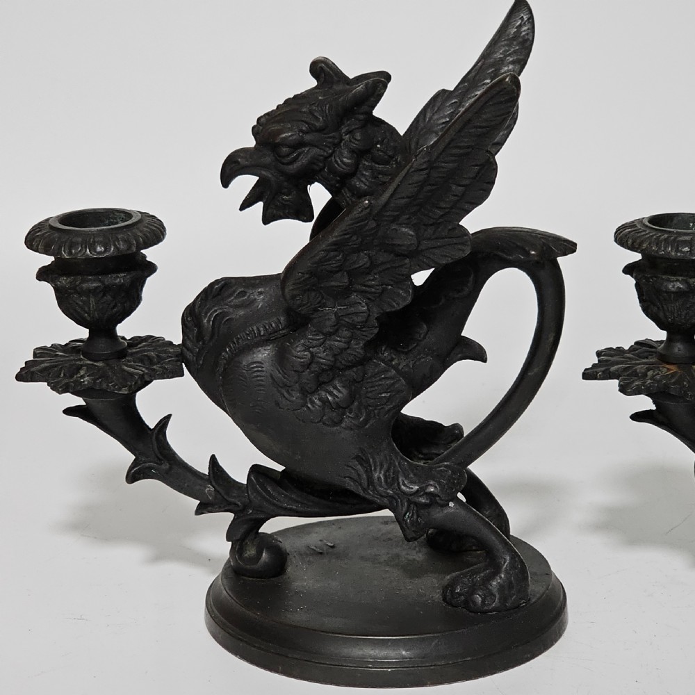 A pair of heavy dark bronze chambersticks featuring mythical griffin figures holding candle nozzles. View XX