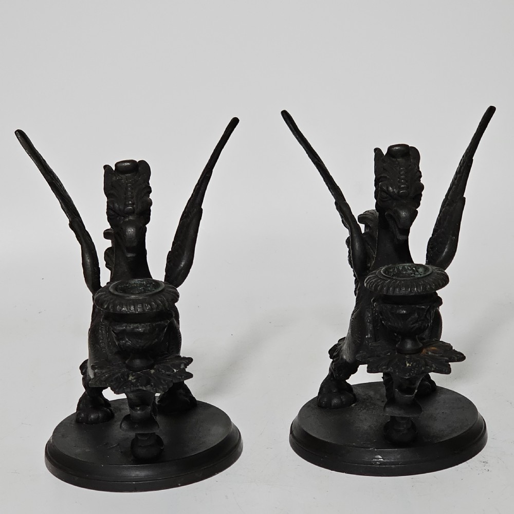 A pair of heavy dark bronze chambersticks featuring mythical griffin figures holding candle nozzles. View XXI