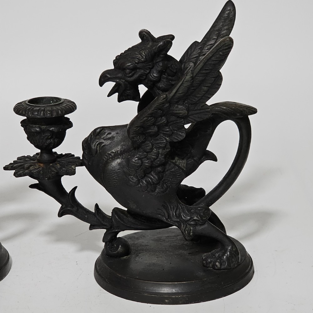 A pair of heavy dark bronze chambersticks featuring mythical griffin figures holding candle nozzles. View XXII