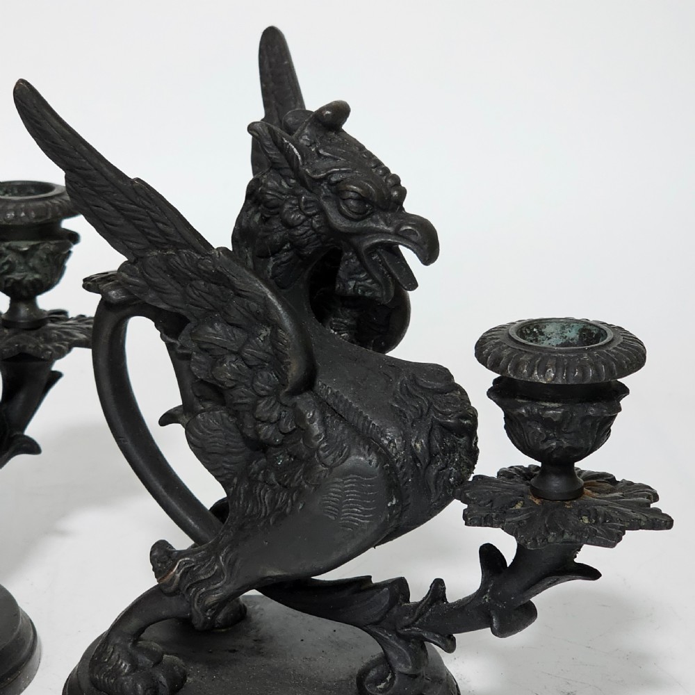 A pair of heavy dark bronze chambersticks featuring mythical griffin figures holding candle nozzles. View XXIII