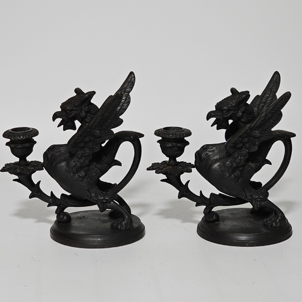 A pair of heavy dark bronze chambersticks featuring mythical griffin figures holding candle nozzles. View XXIV