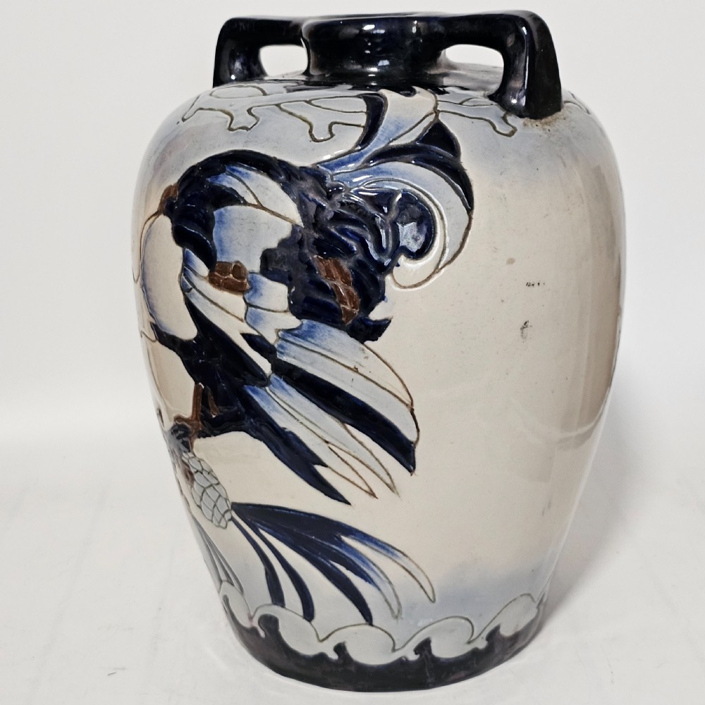 A twin-handled cream ceramic Amphora vase decorated with a stylized bird motif in blue and dark glazes. View X