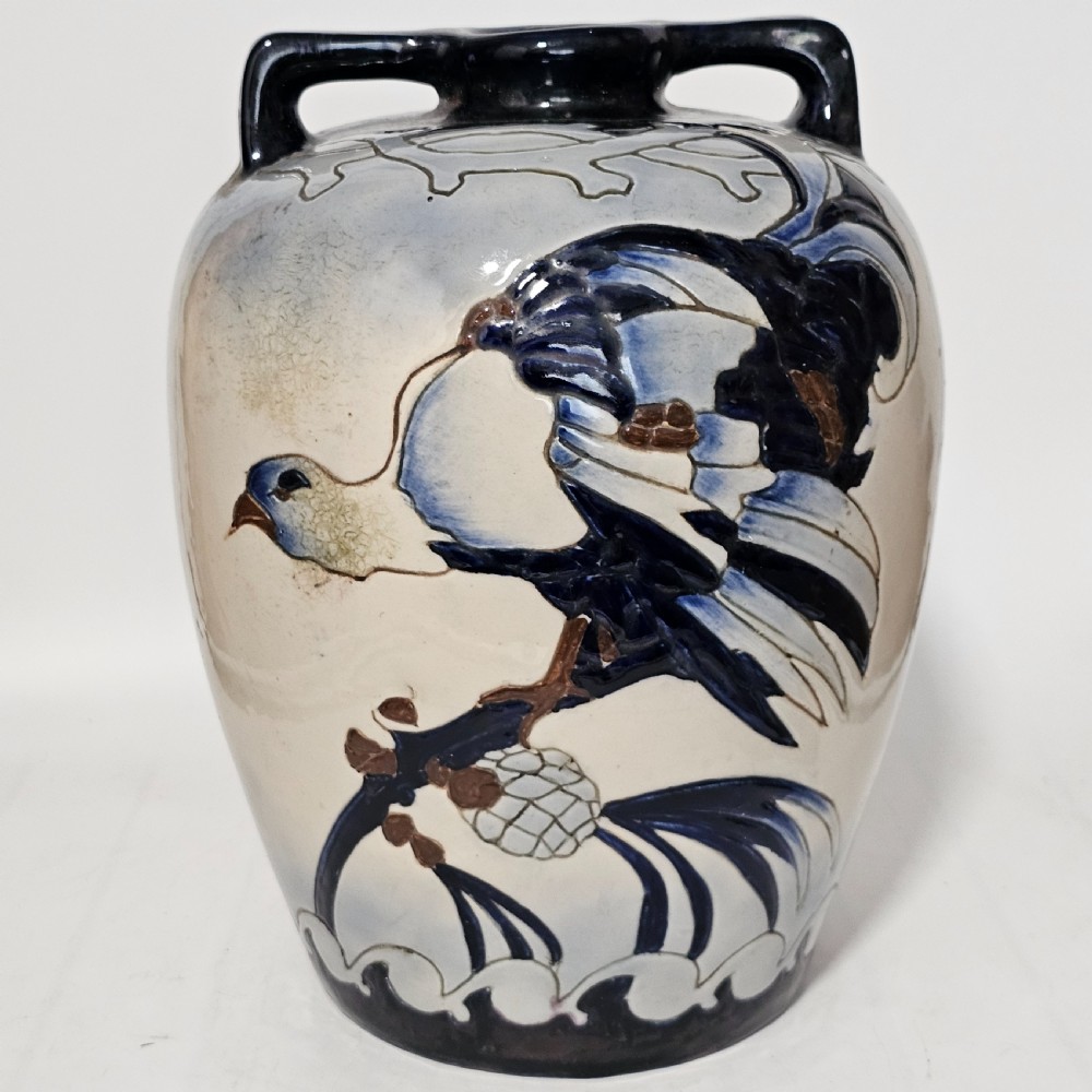 A twin-handled cream ceramic Amphora vase decorated with a stylized bird motif in blue and dark glazes.