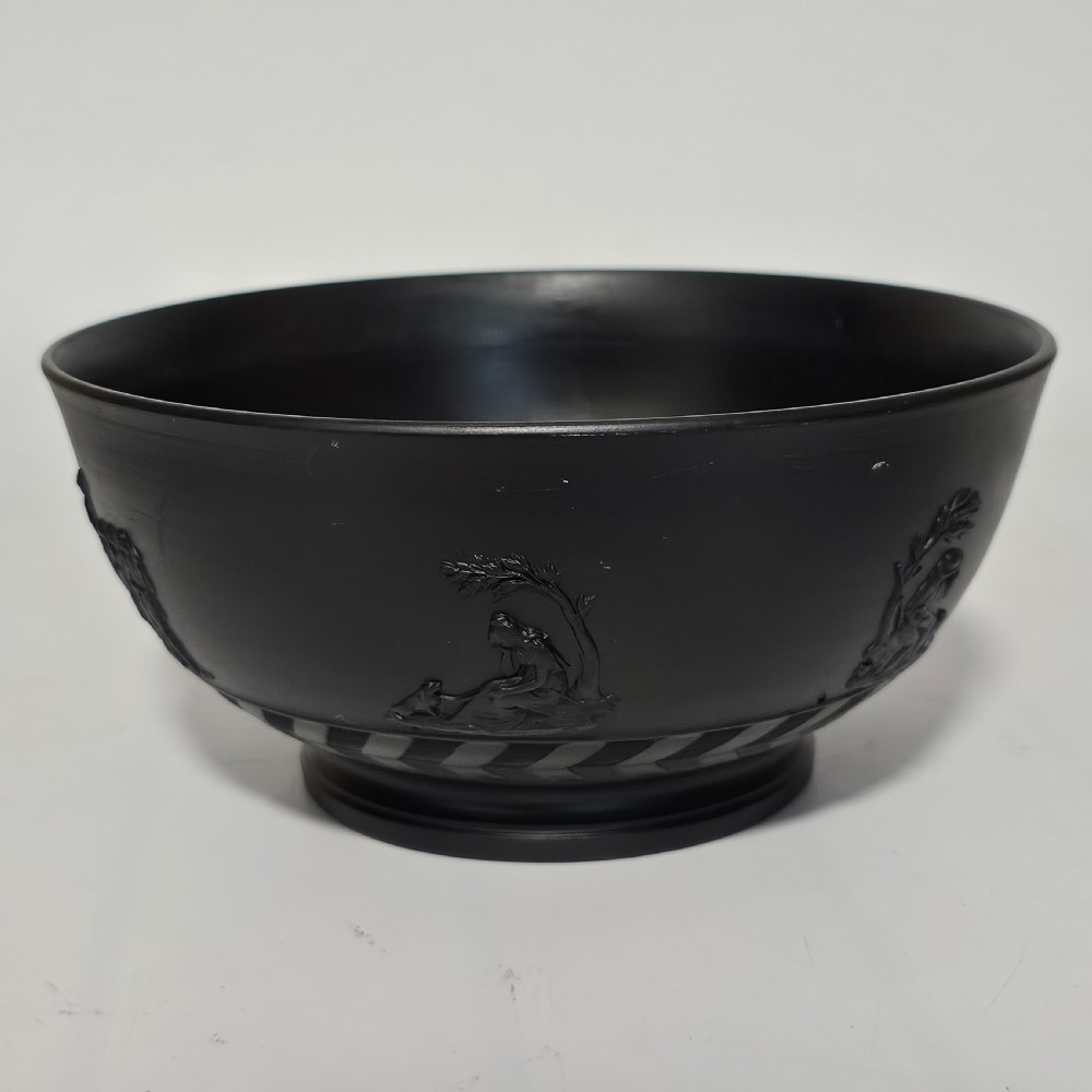 An antique matte black basalt stoneware bowl featuring classical figures in relief around the body and an engine-turned border above the circular foot.