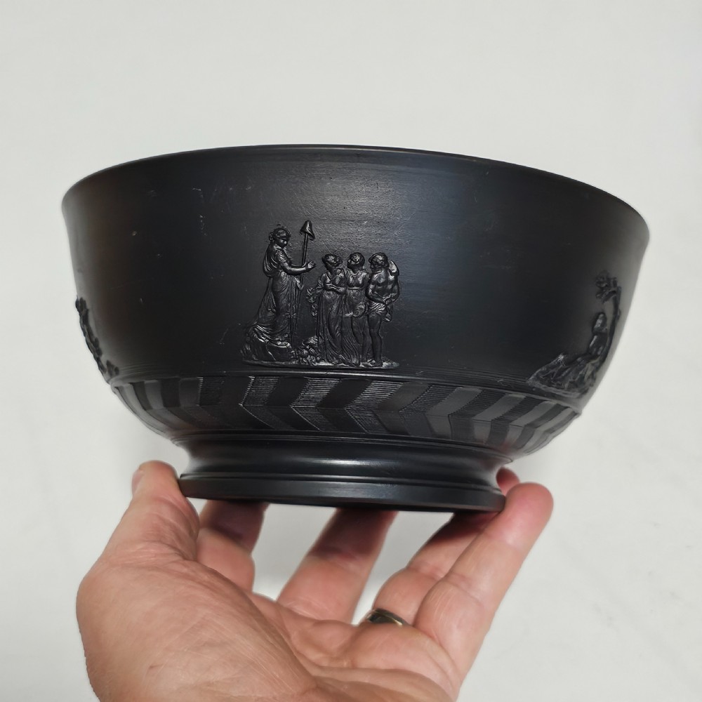 An antique matte black basalt stoneware bowl featuring classical figures in relief around the body and an engine-turned border above the circular foot. View II