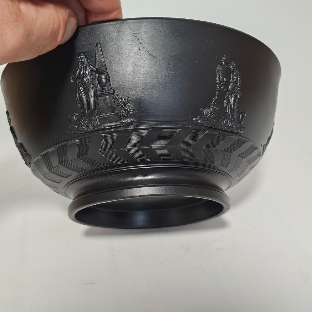 An antique matte black basalt stoneware bowl featuring classical figures in relief around the body and an engine-turned border above the circular foot. View X