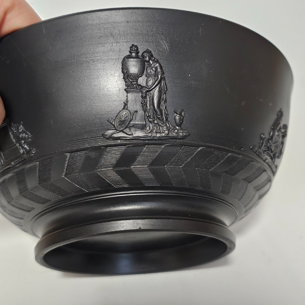 An antique matte black basalt stoneware bowl featuring classical figures in relief around the body and an engine-turned border above the circular foot. View XIV