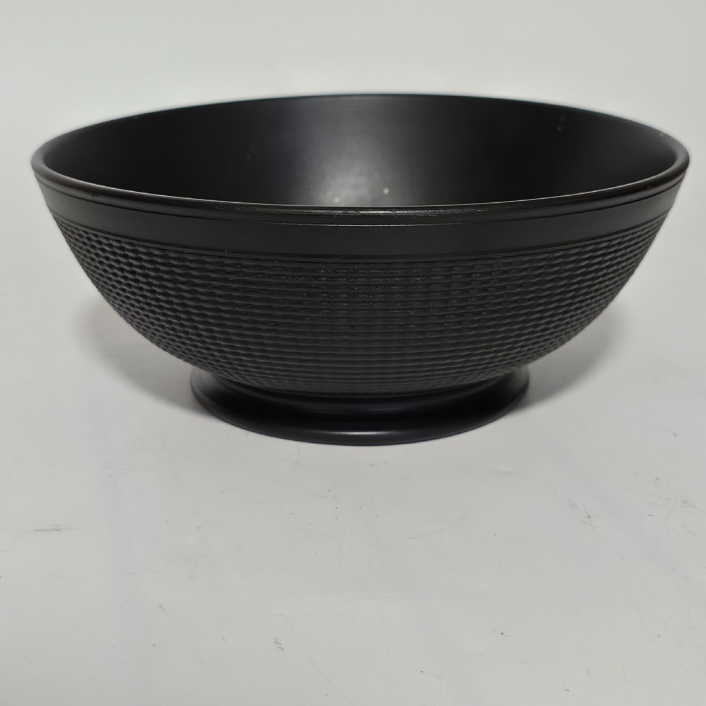 A large matte black basalt stoneware bowl with a textured pattern around the lower body and a circular foot.