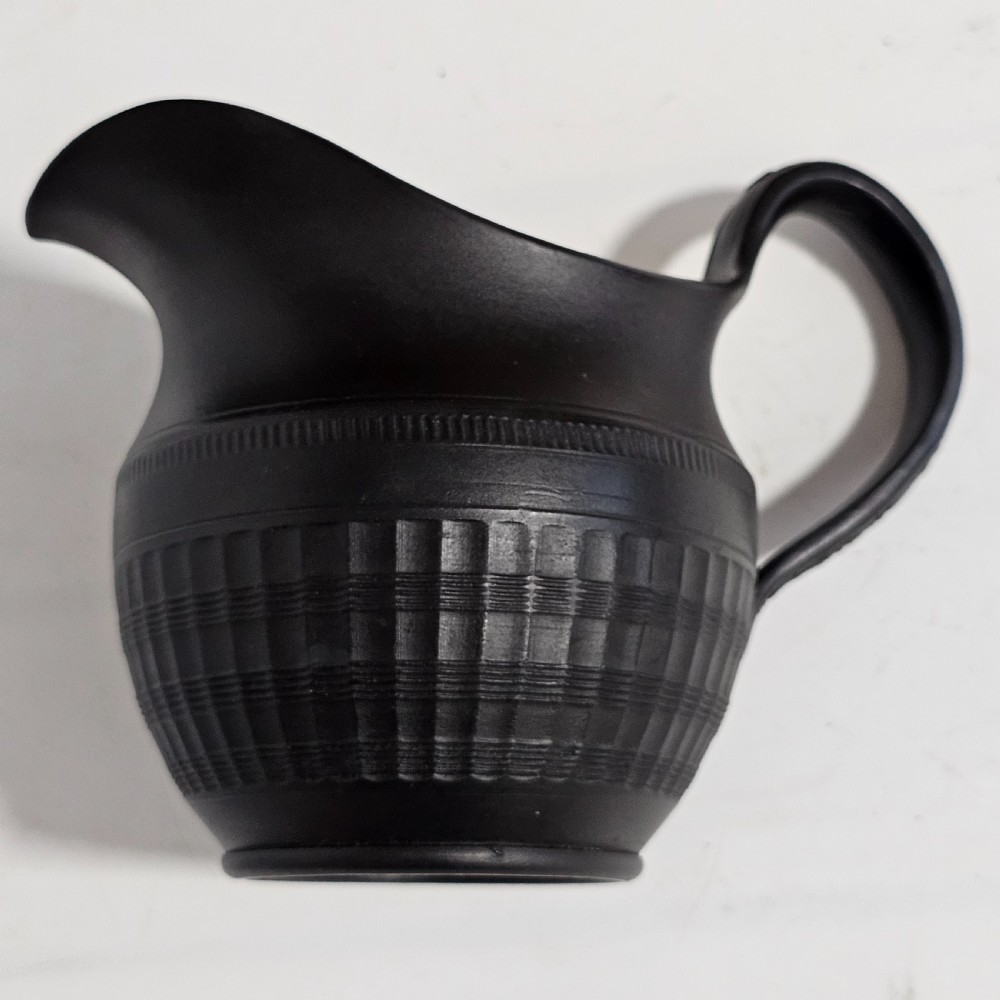 A dark matte black stoneware cream jug featuring incised geometric and reeded bands with a curved handle and pointed pouring spout.