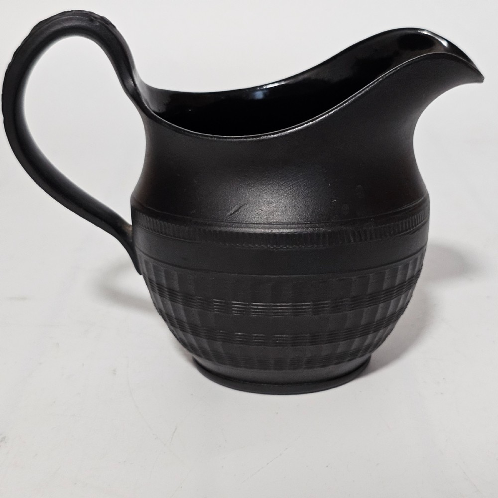 A dark matte black stoneware cream jug featuring incised geometric and reeded bands with a curved handle and pointed pouring spout. View VIII