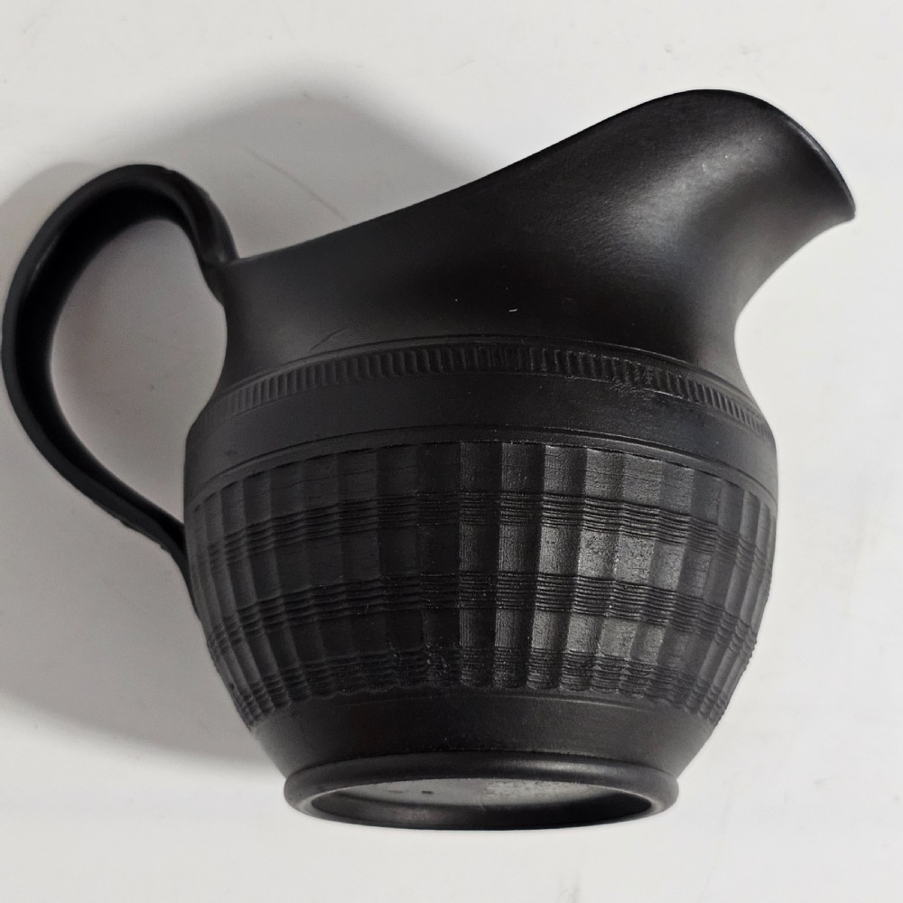 A dark matte black stoneware cream jug featuring incised geometric and reeded bands with a curved handle and pointed pouring spout. View X