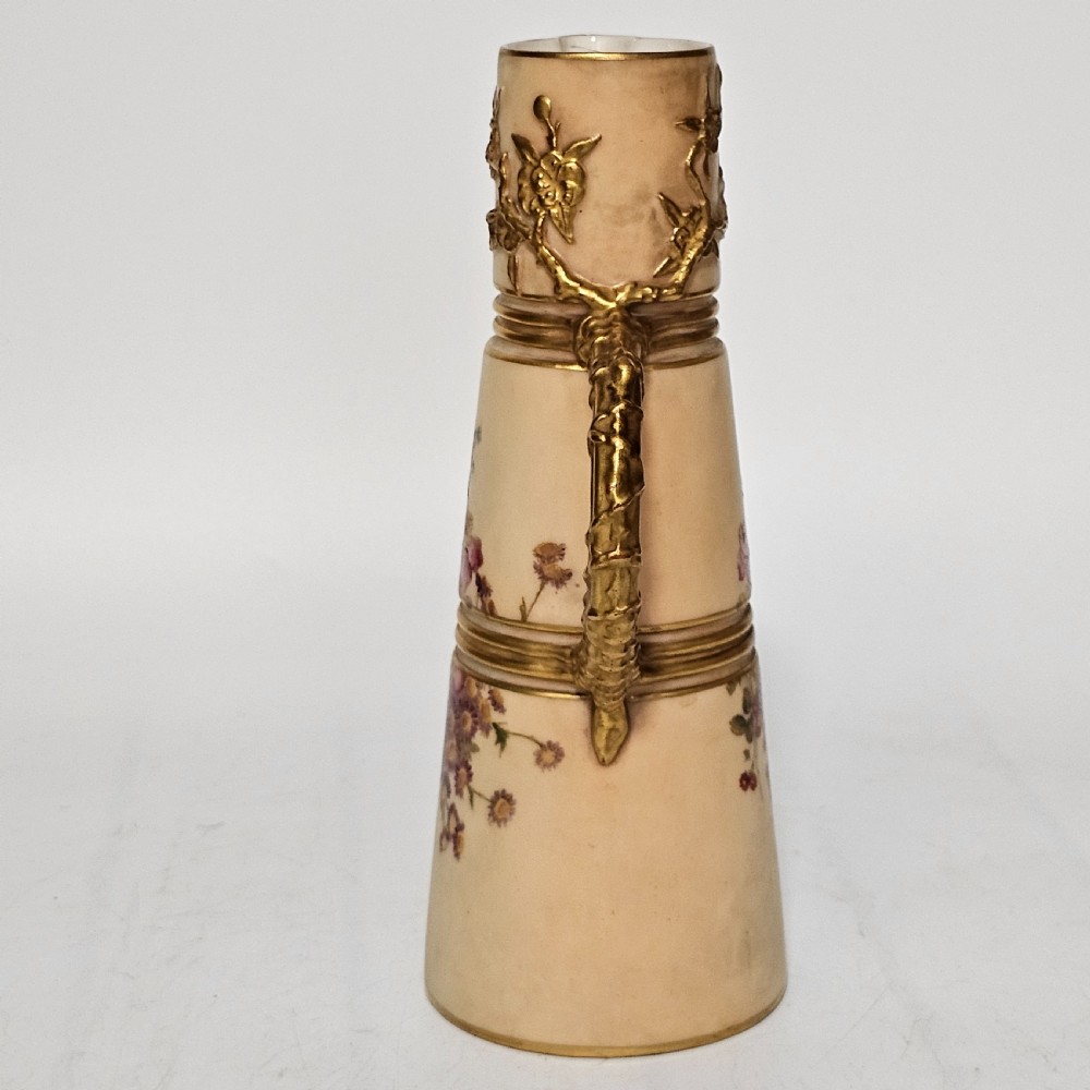A Royal Worcester blush ivory porcelain ewer featuring hand-painted floral motifs, a gilt textured handle, and raised gold blossom decoration on the neck. View II