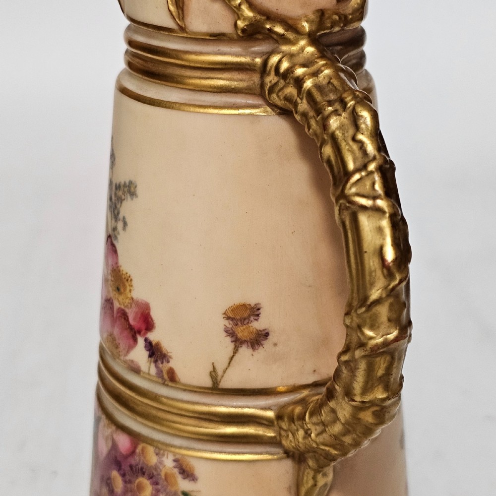 A Royal Worcester blush ivory porcelain ewer featuring hand-painted floral motifs, a gilt textured handle, and raised gold blossom decoration on the neck. View VIII