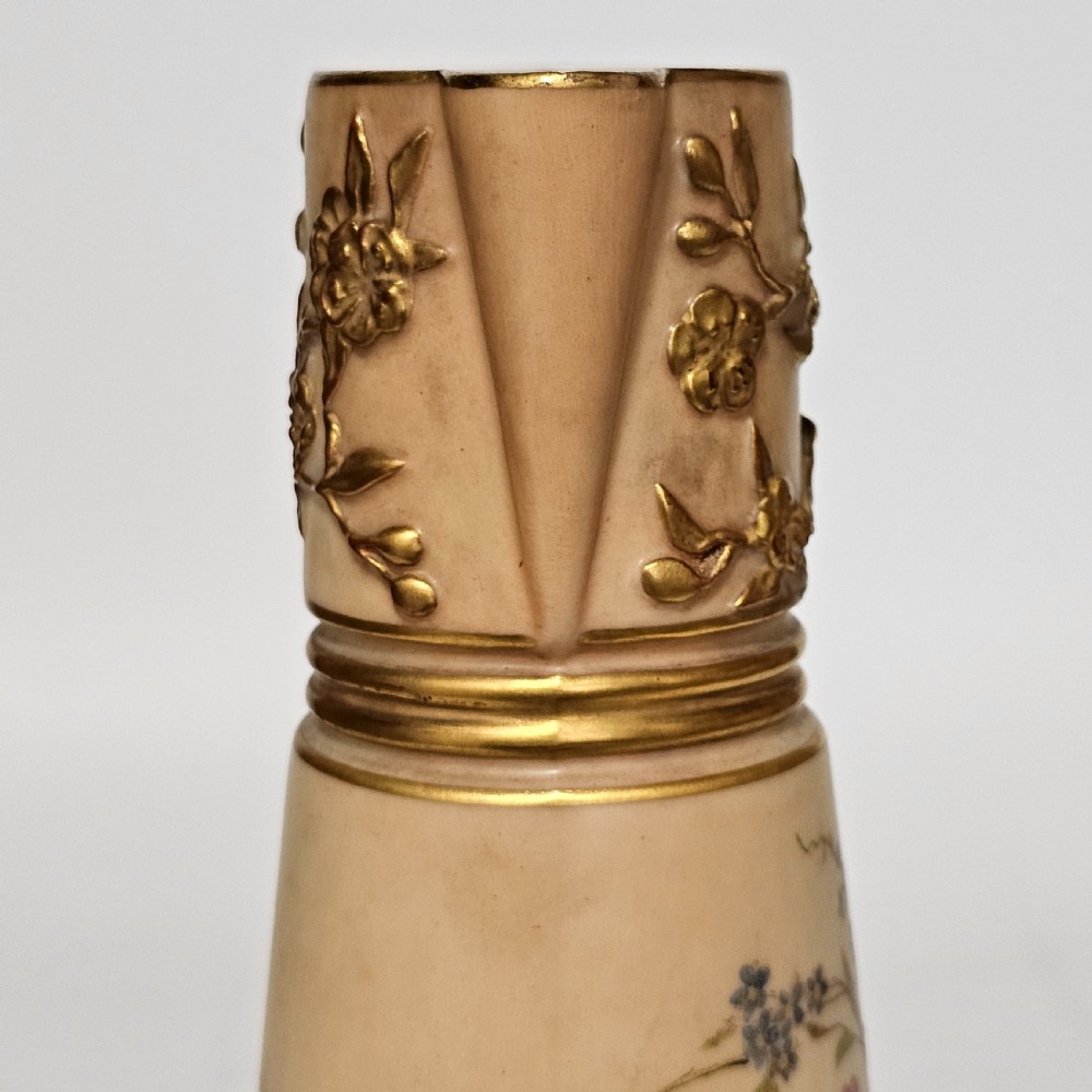 A Royal Worcester blush ivory porcelain ewer featuring hand-painted floral motifs, a gilt textured handle, and raised gold blossom decoration on the neck. View X