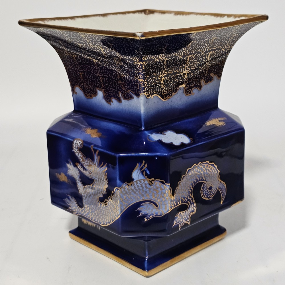 A flared hexagonal cobalt blue porcelain vase decorated with a gilded dragon motif and gold rim.